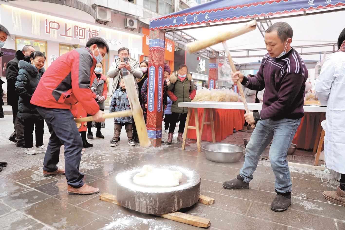 12月26日,鹤峰县容美步行街非遗展台,市民体验打糍粑.