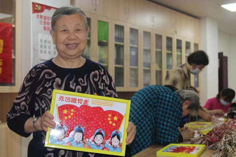 "今年是建党100周年,我们要把亲手制作的这幅手工扣子画送给社区,作为